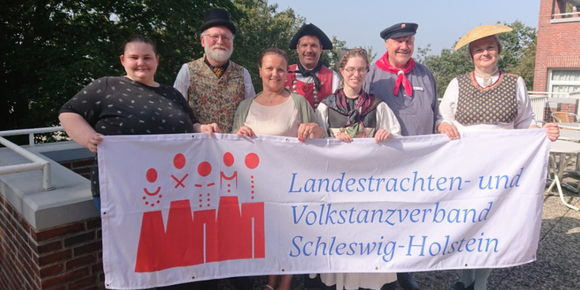 Sieben Personen mit Banner "Landestrachten- und Volkstanzverband Schleswig-Holstein"