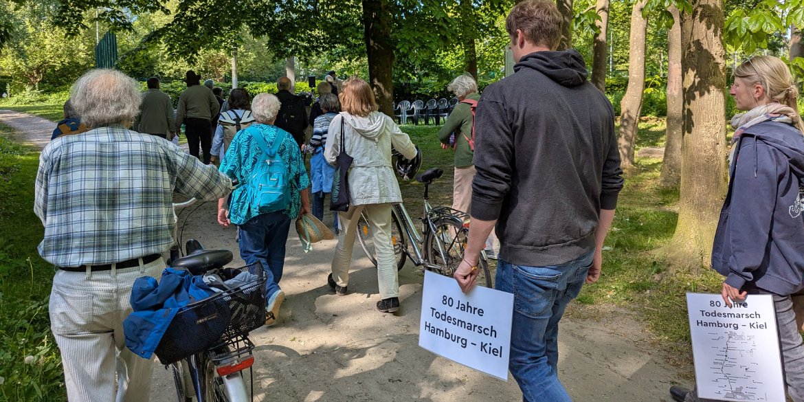 Menschen bei Gedenkwanderung mit Schildern 