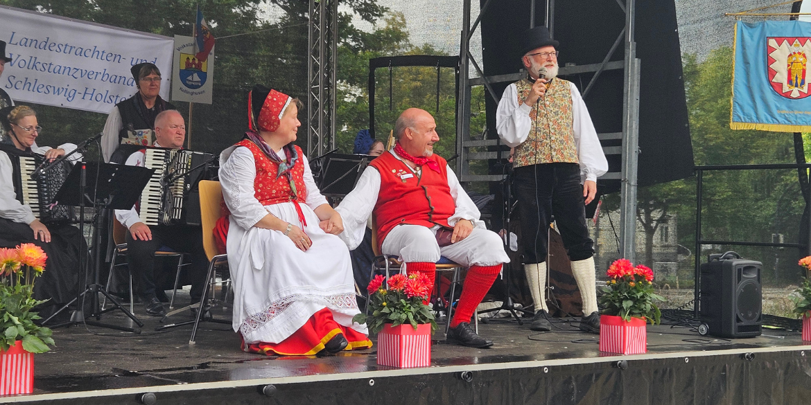 Band und drei Personen in Tracht auf der Bühne