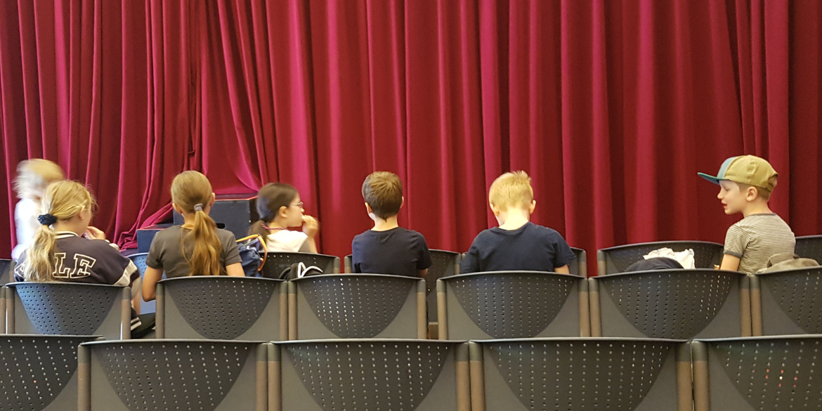 Kinder vor dem geschlossenen Vorhang im Zuschauerraum des Theaters