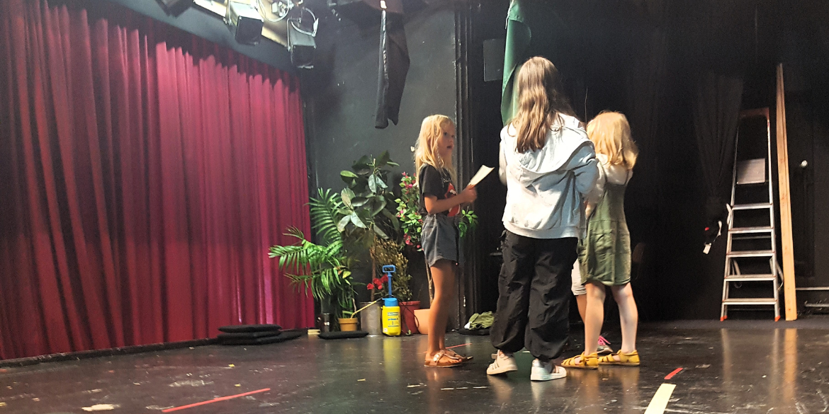 Drei Kinder stehen auf der Theaterbühne im Kreis