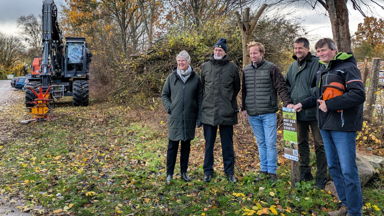 Gruppe von fünf Personen und Bagger mit Knickschere vor frisch geknicktem Knick