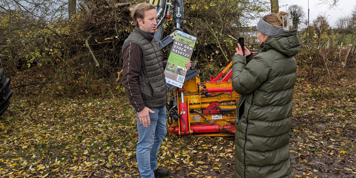 Person mit Schild vor Knickschere und Person der Presse, die Foto macht
