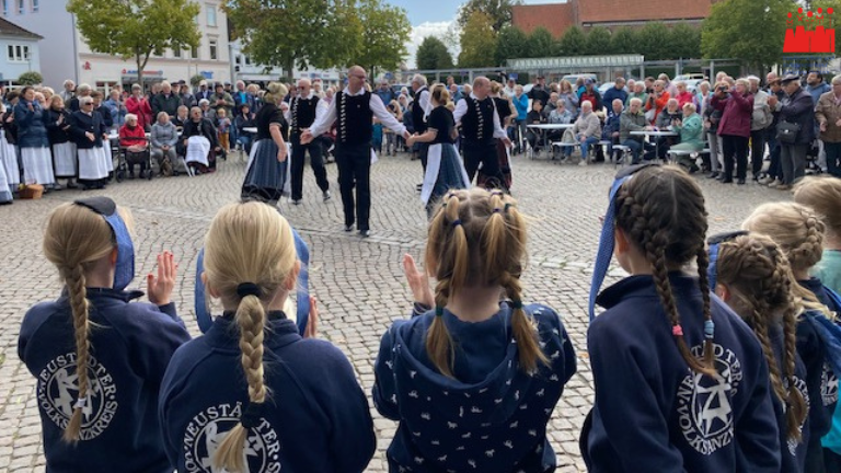 Tänzer*innen in Tracht auf Marktplatz umringt von Publikum