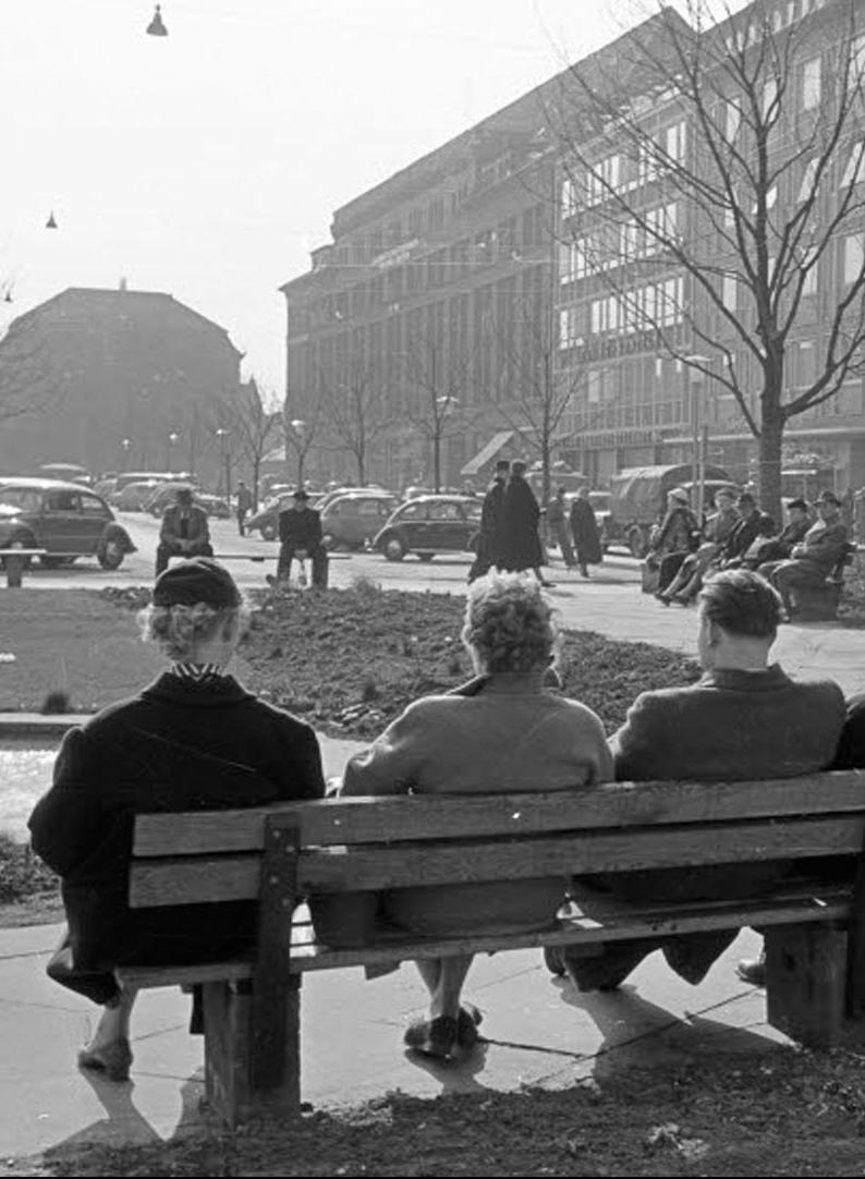 Historisches Bild: Drei Personen sitzen an einem Platz in der Stadt auf einer Bank
